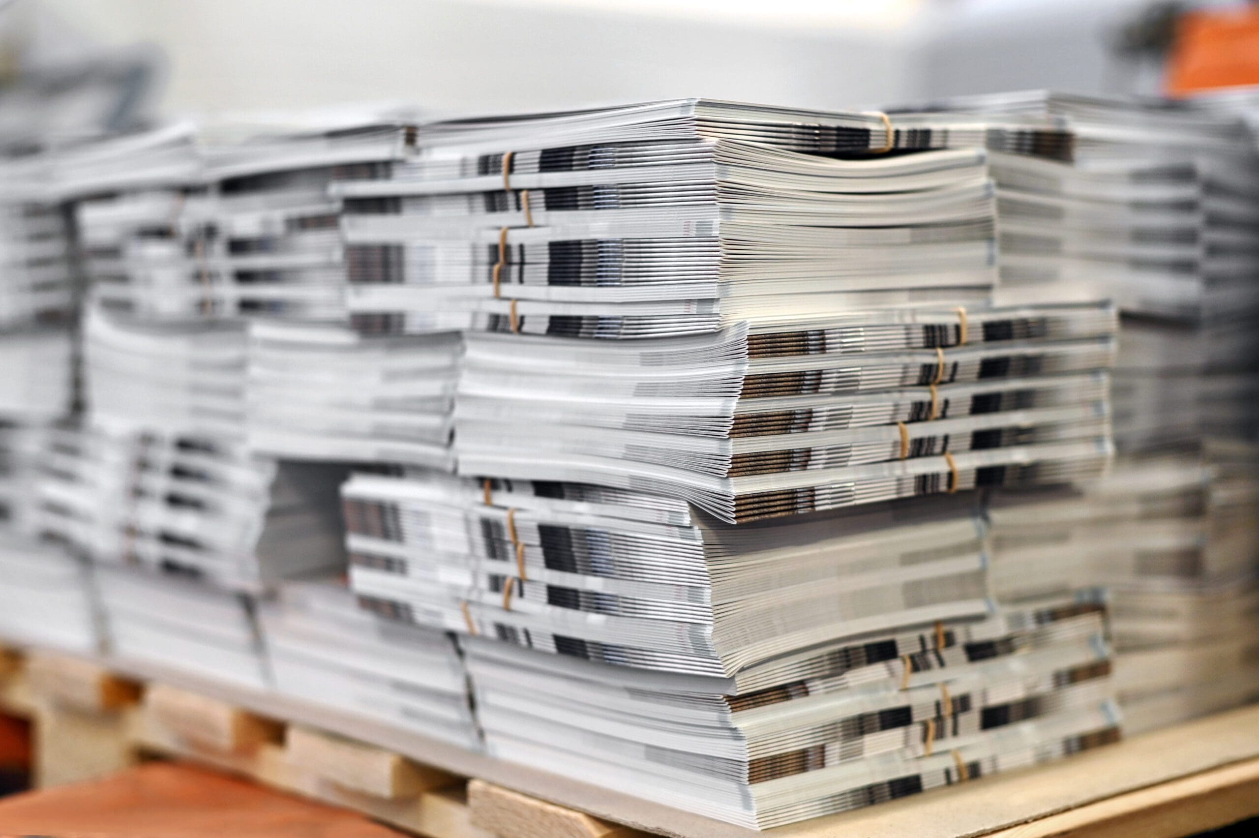 Soft focus of sheets of freshly printed catalogs stacked together on wooden pallet in typography workshop